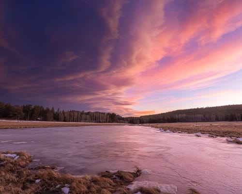 Sunset painting an altocumulus standing lenticular cloud wall over a frozen pond in the foothills of Colorado